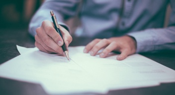 Persona escrivint en una fulla de paper amb un bolígraf